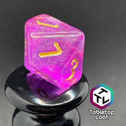 A close up of the D10 from the Moxie 7 piece dice set from Tabletop Loot; fuchsia dice packed with glitter and gold gothic numbering.