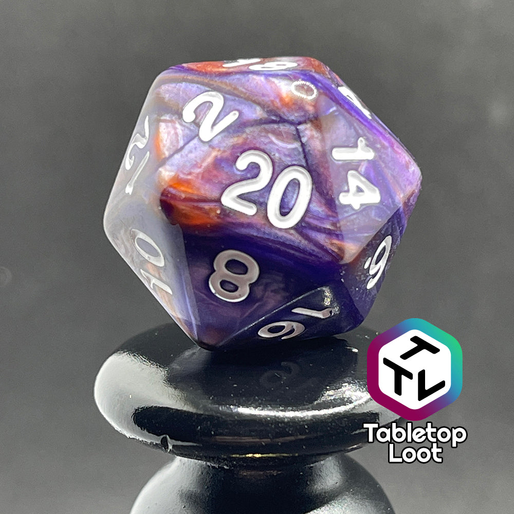 A close up of the D20 from the Mystical Aura 7 piece dice set from Tabletop Loot with swirls of iridescent blue, purple, and orange and white numbering.