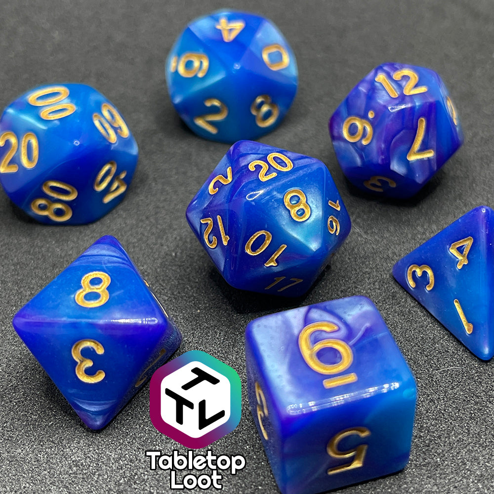 The Mystique 7 piece dice set from Tabletop Loot with swirls of purple in pearlescent blue and gold numbering.