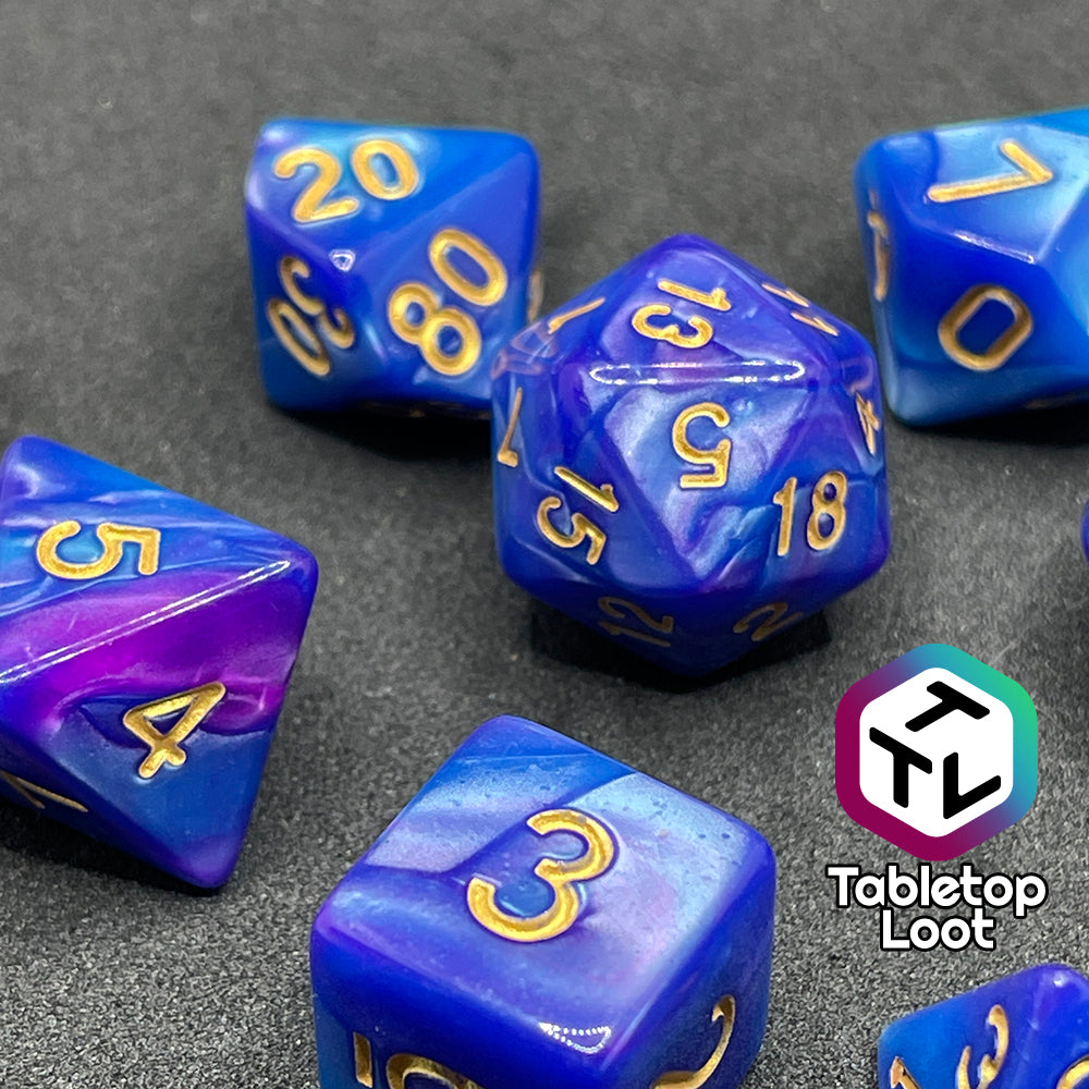 The Mystique 7 piece dice set from Tabletop Loot with swirls of purple in pearlescent blue and gold numbering.