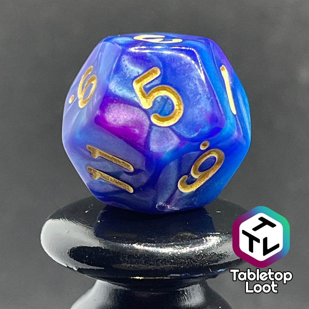 A close up of the D12 from the Mystique 7 piece dice set from Tabletop Loot with swirls of purple in pearlescent blue and gold numbering.