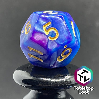 A close up of the D12 from the Mystique 7 piece dice set from Tabletop Loot with swirls of purple in pearlescent blue and gold numbering.