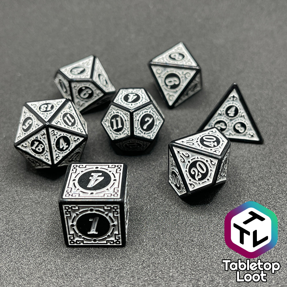 The Necromancer's Thrall 7 piece dice set from Tabletop Loot with bold white numbers on intricate scrolling black frames that make up each side.