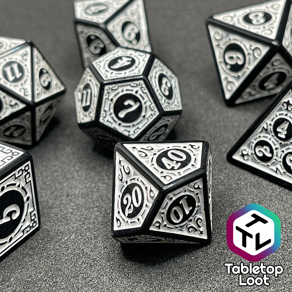 A close up of the Necromancer's Thrall 7 piece dice set from Tabletop Loot with bold white numbers on intricate scrolling black frames that make up each side.