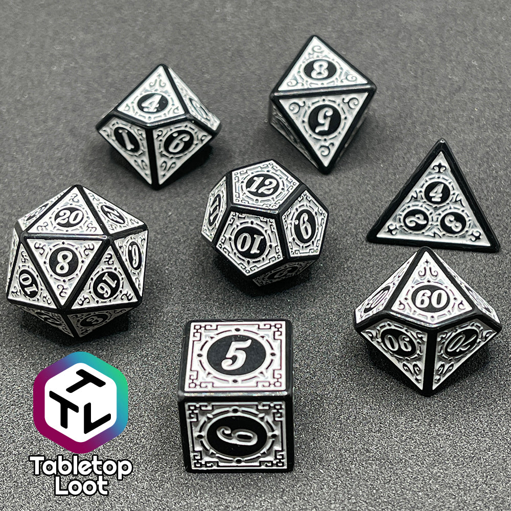 A close up of the Necromancer's Thrall 7 piece dice set from Tabletop Loot with bold white numbers on intricate scrolling black frames that make up each side.