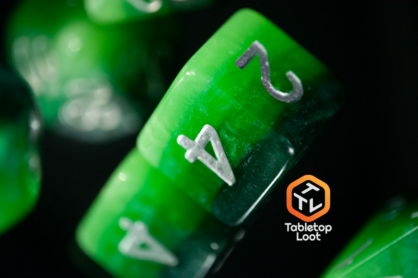 A close up of the Necropolis D6 from Tabletop Loot with stripes of four shades of glittery green resin and silver numbering.