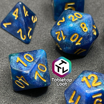 A close up of the Neptune's Grace 7 piece dice set from Tabletop Loot with swirls of shimmery blue, hints of green , and gold numbering.