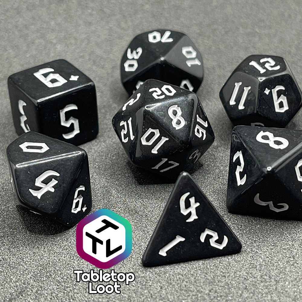 A close up of the Nevermore 7 piece dice set from Tabletop Loot with white gothic numbering on highly polished black faces.