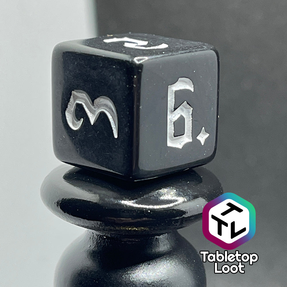 A close up of the D6 from the Nevermore 7 piece dice set from Tabletop Loot with white gothic numbering on highly polished black faces.