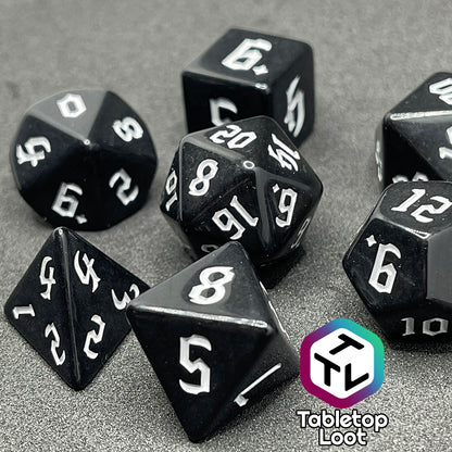A close up of the Nevermore 7 piece dice set from Tabletop Loot with white gothic numbering on highly polished black faces.