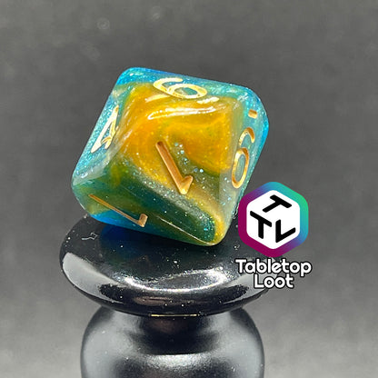 A close up of the D10 from the Nimrodel 7 piece dice set from Tabletop Loot with swirls of glittering blue, green, and orange and golden numbering.