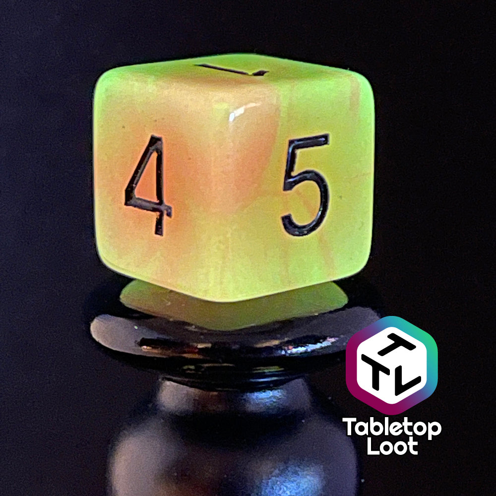 A close up of the D6 from the Nuclear glow in the dark 7 piece dice set from Tabletop Loot with swirls of orange and yellow glow pigment and black numbering, shown glowing.