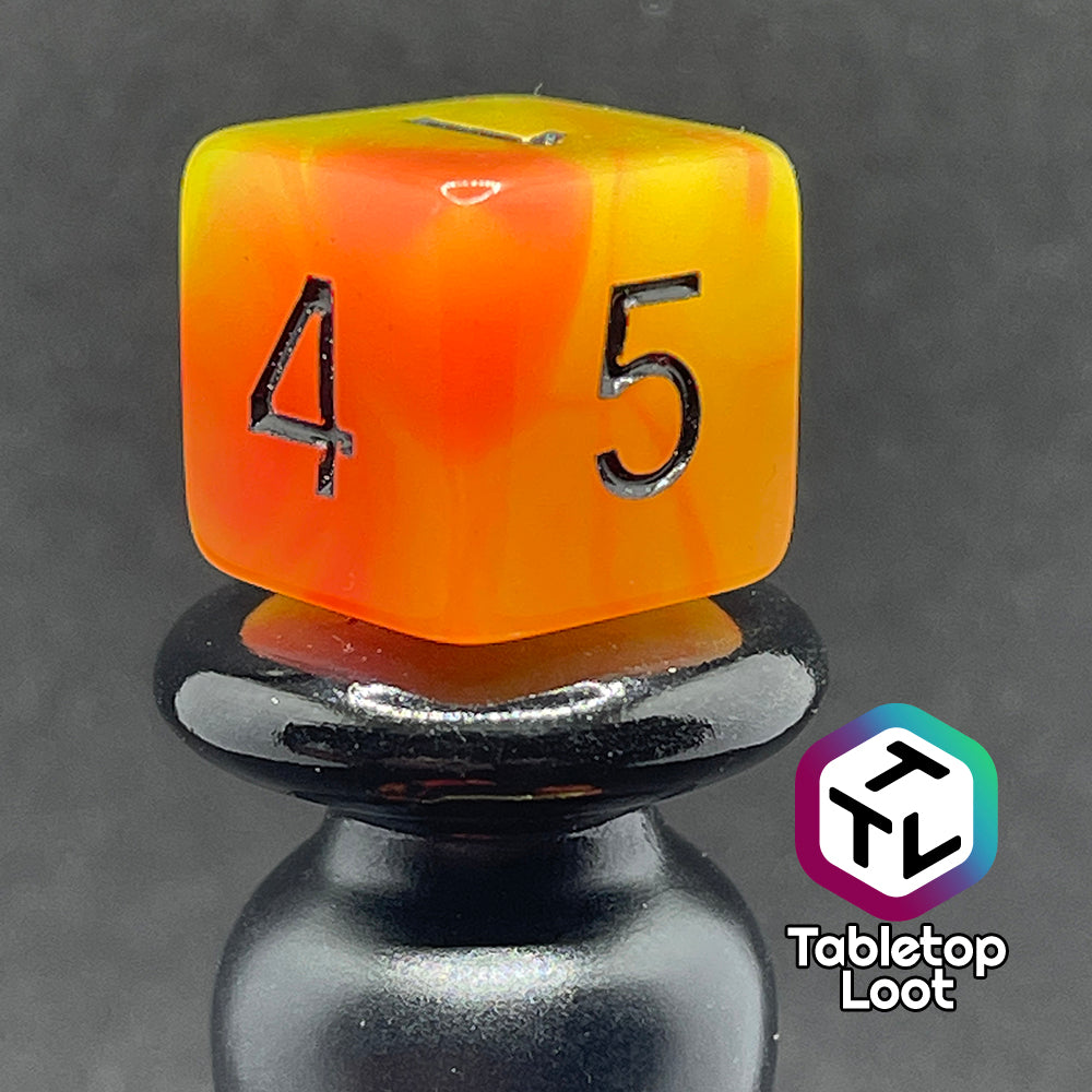A close up of the D6 from the Nuclear glow in the dark 7 piece dice set from Tabletop Loot with swirls of orange and yellow glow pigment and black numbering, shown in light.