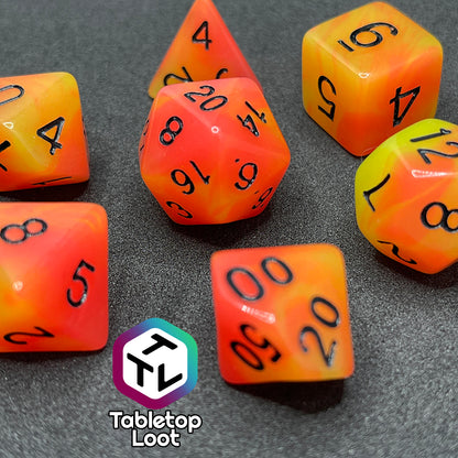 A close up of the Nuclear glow in the dark 7 piece dice set from Tabletop Loot with swirls of orange and yellow glow pigment and black numbering, shown in light.