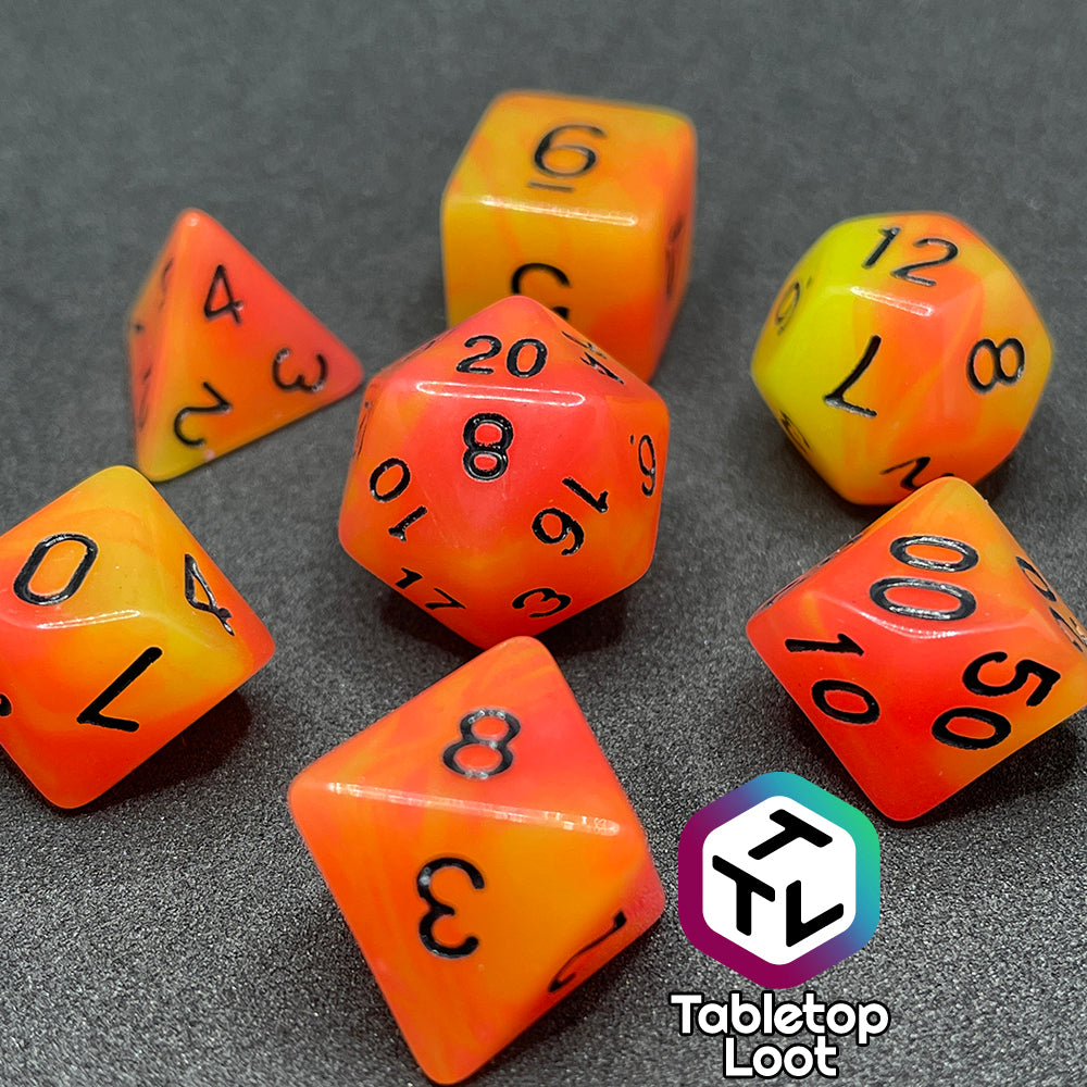 The Nuclear glow in the dark 7 piece dice set from Tabletop Loot with swirls of orange and yellow glow pigment and black numbering, shown in light.