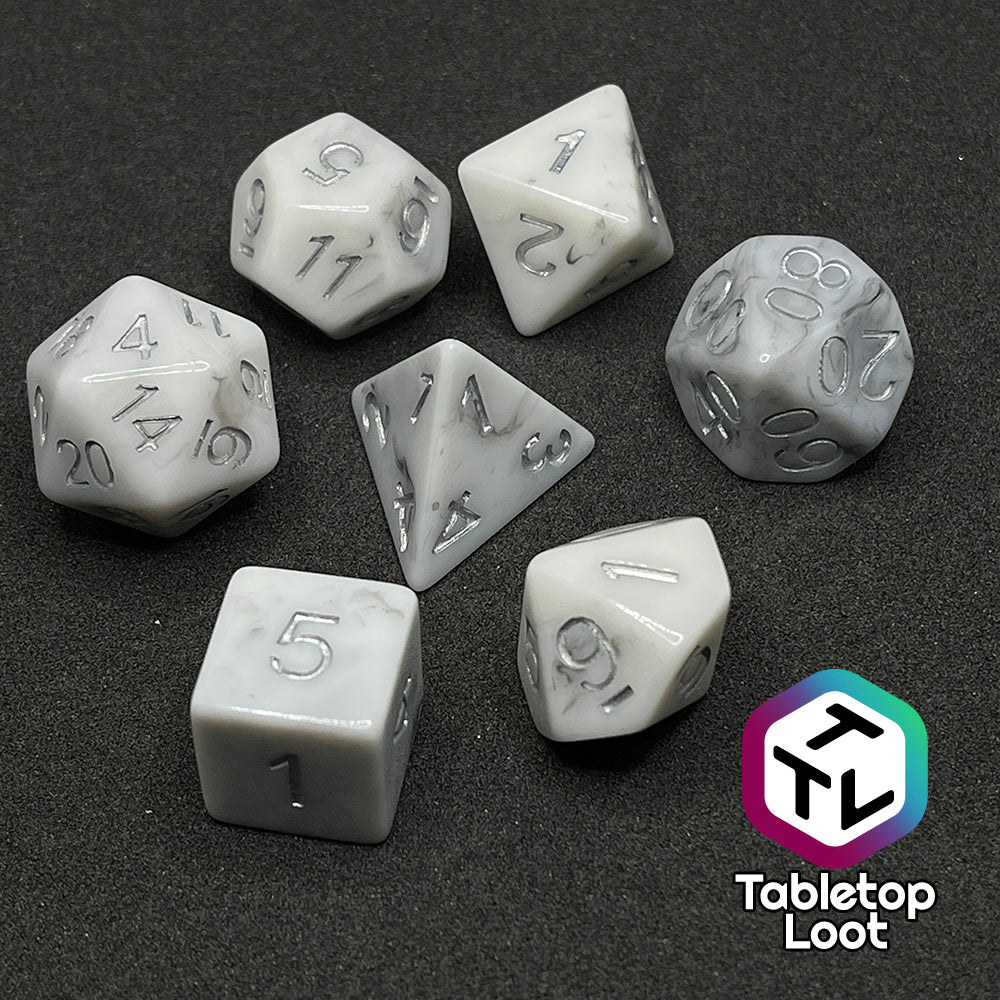 The Oath Breaker 7 piece dice set from Tabletop Loot; opaque white with swirls of silver peeking out and silver numbering.