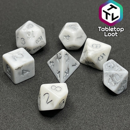 The Oath Breaker 7 piece dice set from Tabletop Loot; opaque white with swirls of silver peeking out and silver numbering.