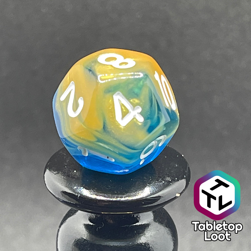 A close up of a different side of the D12 in the Oceanside 7 piece dice set from Tabletop Loot with swirls of glittery yellow and blue suspended in clear acrylic with white numbering.