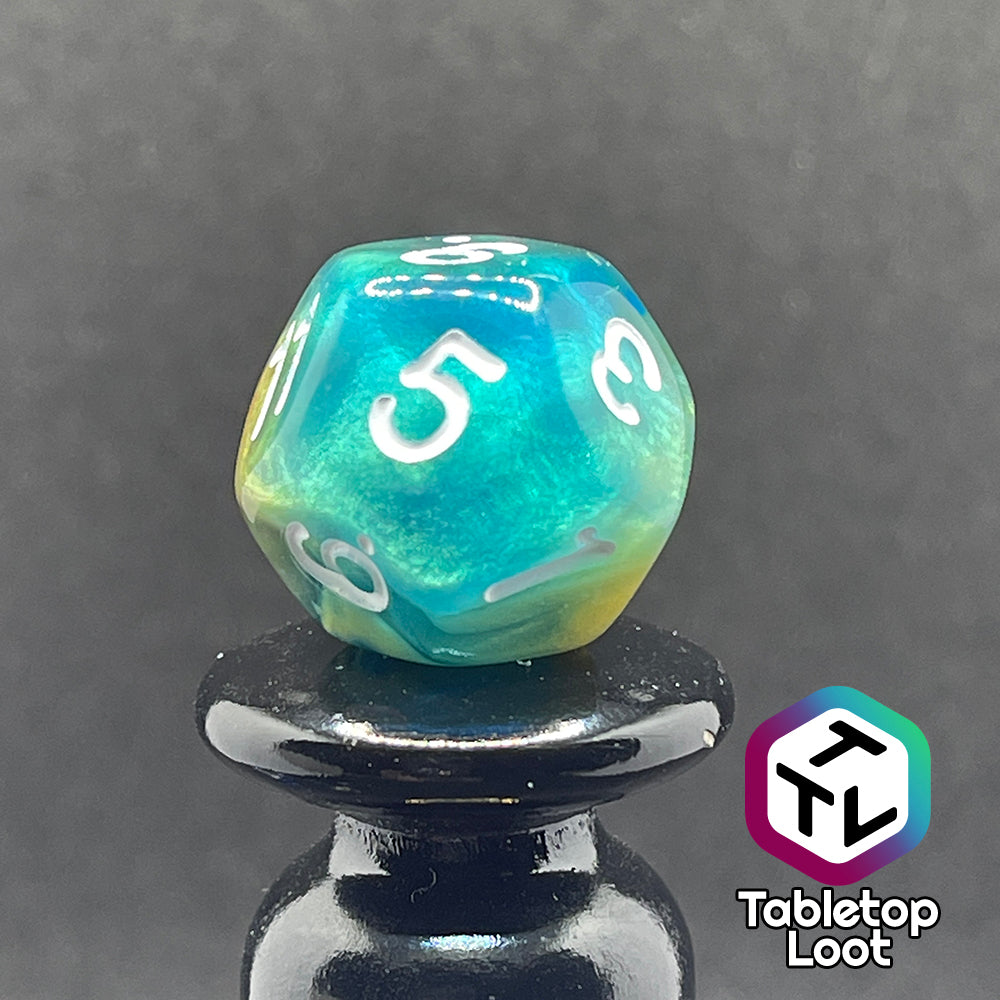 A close up of a different side of the D12 from the Oceanside 7 piece dice set from Tabletop Loot with swirls of glittery yellow and blue suspended in clear acrylic with white numbering.