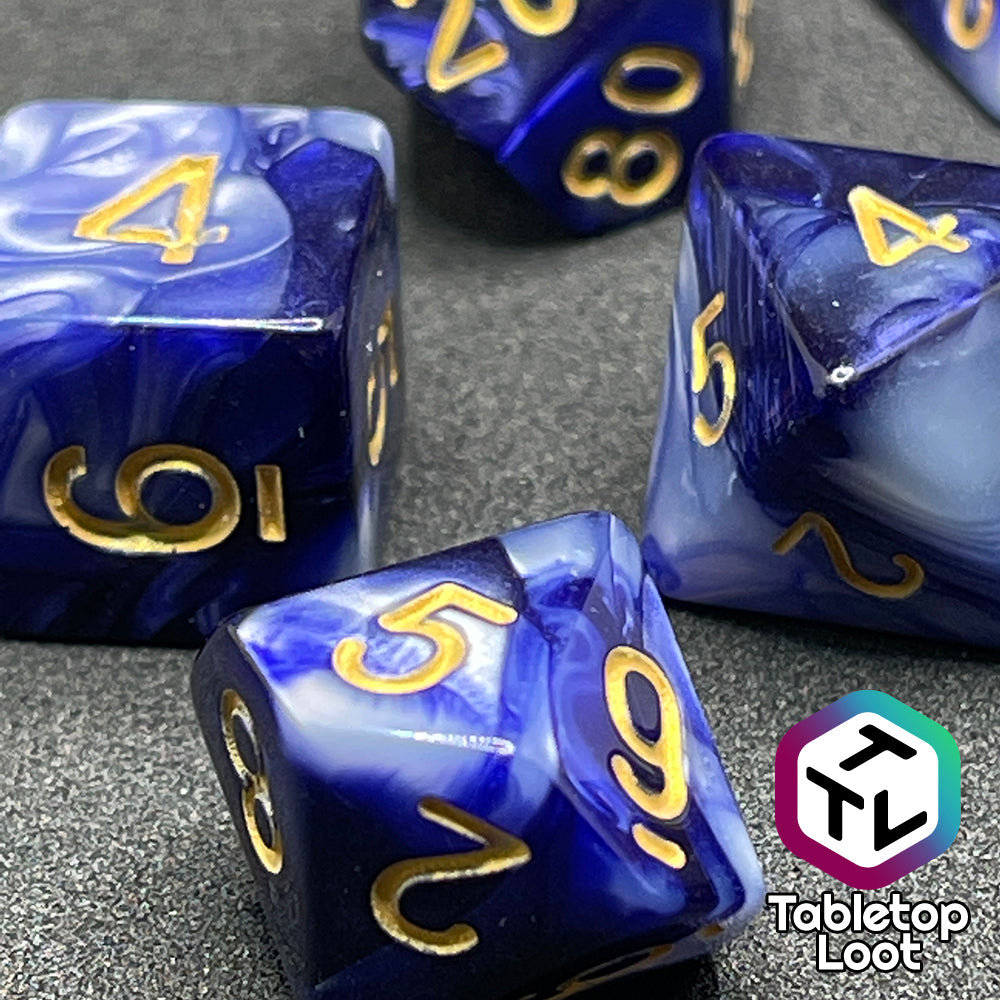 A close up of the D10 and D6 from the Order of the Night's Veil 7 piece dice set from Tabletop Loot with swirls of pearlescent purple and white with gold numbering.