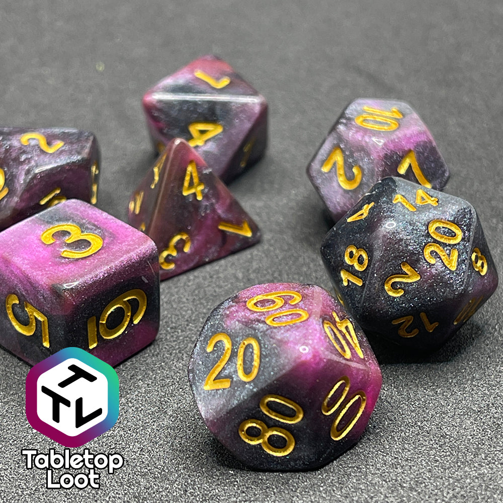 A close up of the Orion Nebula 7 piece dice set from Tabletop Loot with swirls of pink and black, tons of glitter, and gold numbering.