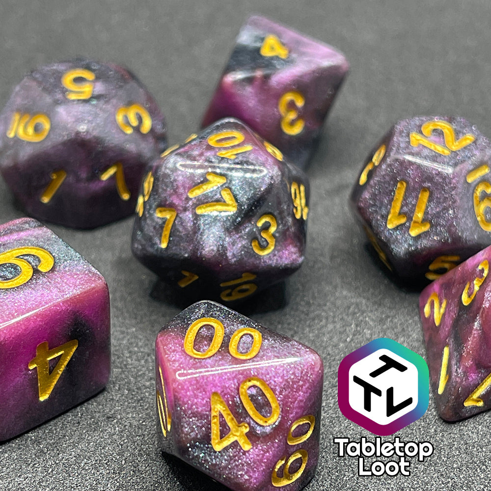 A close up of the Orion Nebula 7 piece dice set from Tabletop Loot with swirls of pink and black, tons of glitter, and gold numbering.