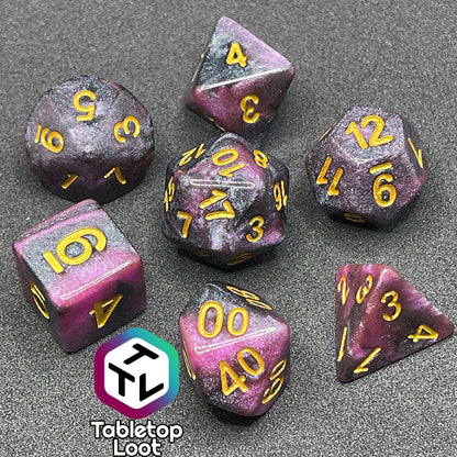 The Orion Nebula 7 piece dice set from Tabletop Loot with swirls of pink and black, tons of glitter, and gold numbering.