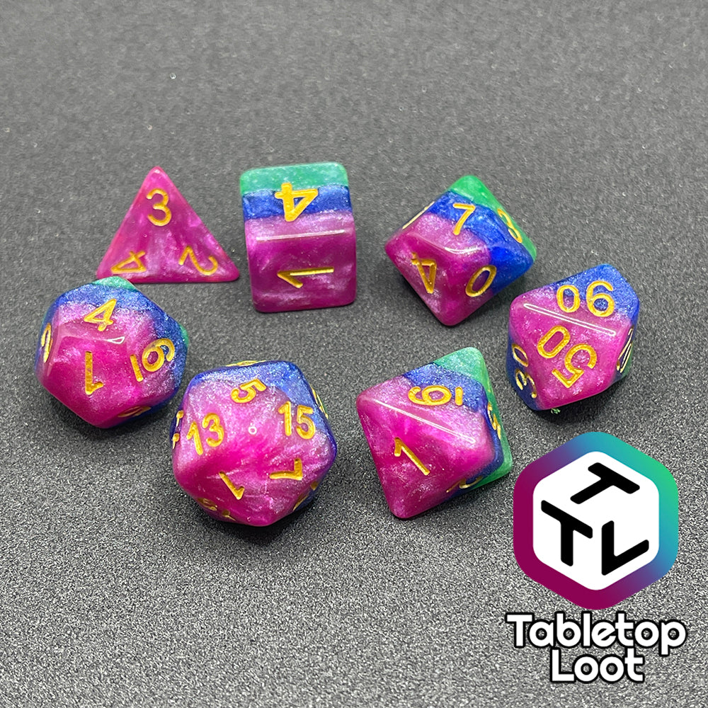 The Petit Fours 7 piece dice set from Tabletop Loot; layers of shimmering green, blue, and pink with gold numbering.