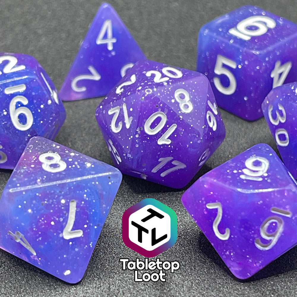 A close up of the Phantasmal Force 7 piece dice set with swirls of blue and purple, lots of glitter, and white numbering.