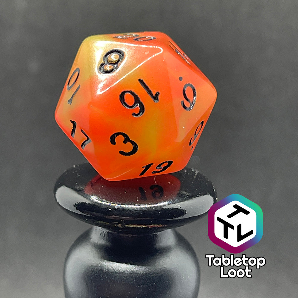 A close up of the D20 from the Neon Nights glow in the dark 7 piece dice set from Tabletop Loot with swirled orange and yellow glow pigment and black numbering, shown in light.