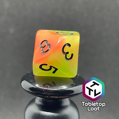 A close up of the percentile die from the Neon Nights glow in the dark 7 piece dice set from Tabletop Loot with swirled orange and yellow glow pigment and black numbering, shown in light.