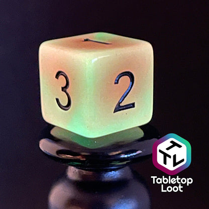 A close up of the D6 from the Neon Nights glow in the dark 7 piece dice set from Tabletop Loot with swirled orange and yellow glow pigment and black numbering, shown glowing.