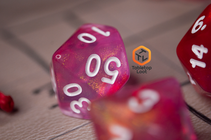 A close up of the Pink Bunny 7 piece dice set from Tabletop Loot with yellow and gold shimmer in bright pink resin with white numbering.