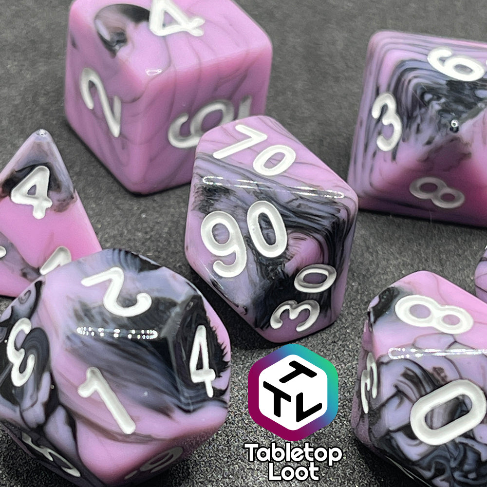 A close up of the Pink Nightmare 7 piece dice set from Tabletop Loot with swirls of black in pink with white numbering.