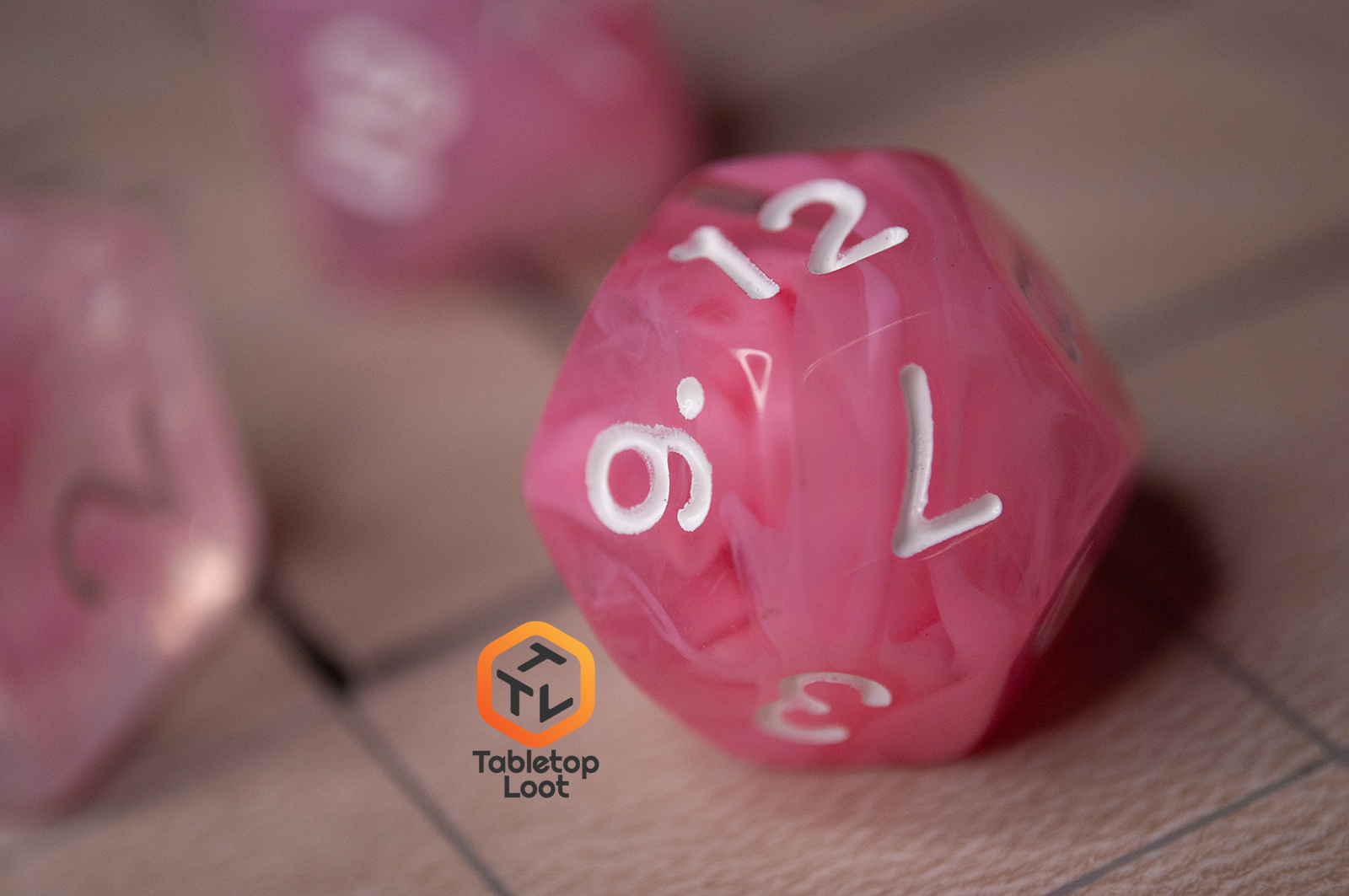 A close up of the D12 from the Pink Rose 7 piece dice set from Tabletop Loot with ribbons of pink in a clear resin with white numbering.