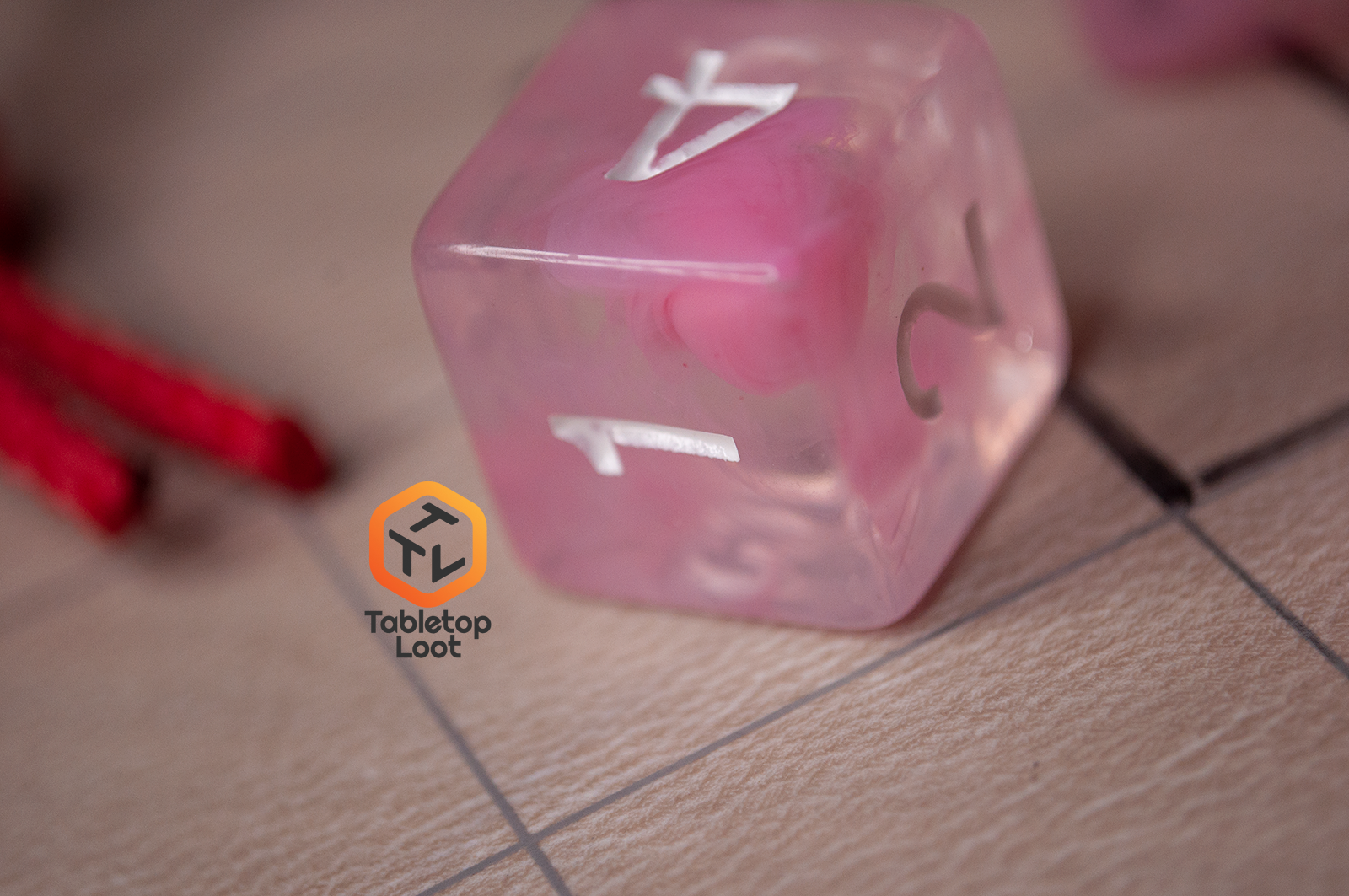 A close up of the D6 from the Pink Rose 7 piece dice set from Tabletop Loot with ribbons of pink in a clear resin with white numbering.