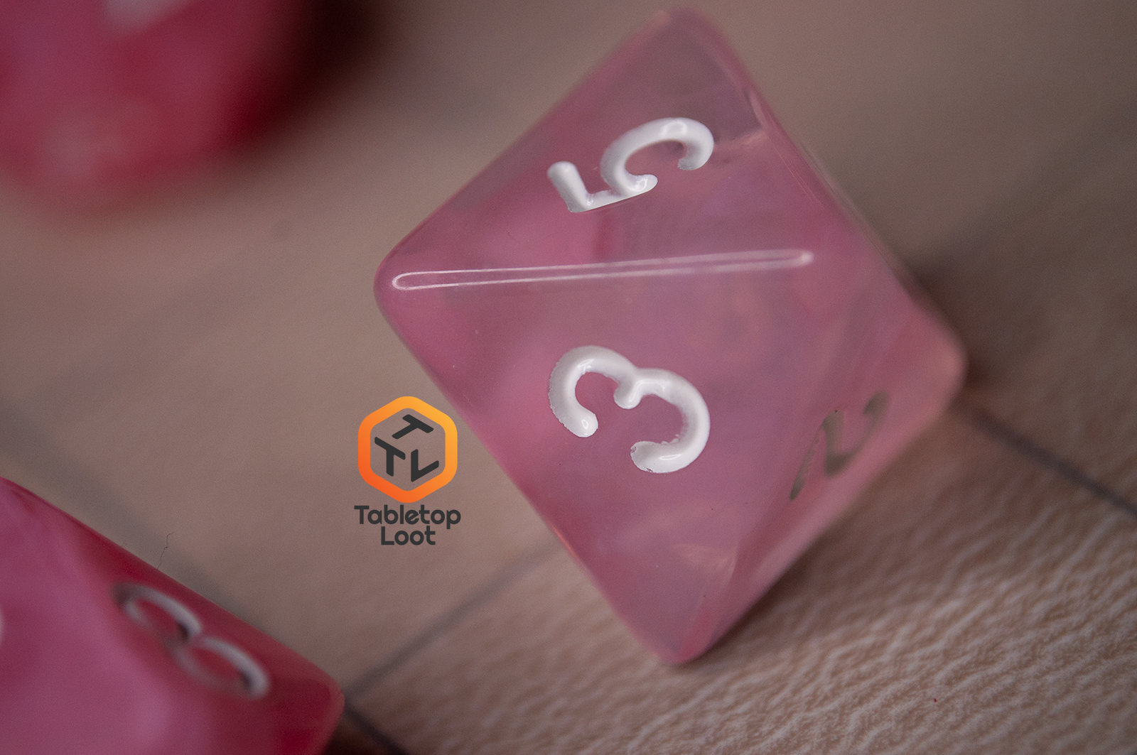 A close up of the D8 from the Pink Rose 7 piece dice set from Tabletop Loot with ribbons of pink in a clear resin with white numbering.