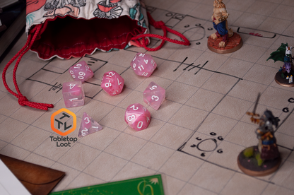 The Pink Rose 7 piece dice set from Tabletop Loot with ribbons of pink in a clear resin with white numbering.