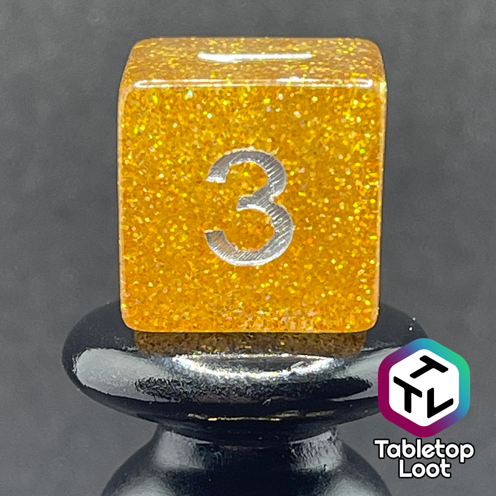 A close up of the D6 from the Pixie Dust 7 piece dice set from Tabletop Loot; gold glittery dice with silver numbering.