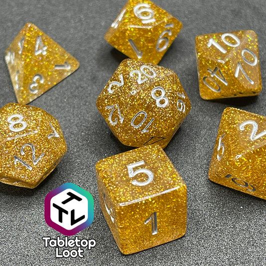 A close up of the Pixie Dust 7 piece dice set from Tabletop Loot; gold glittery dice with silver numbering.