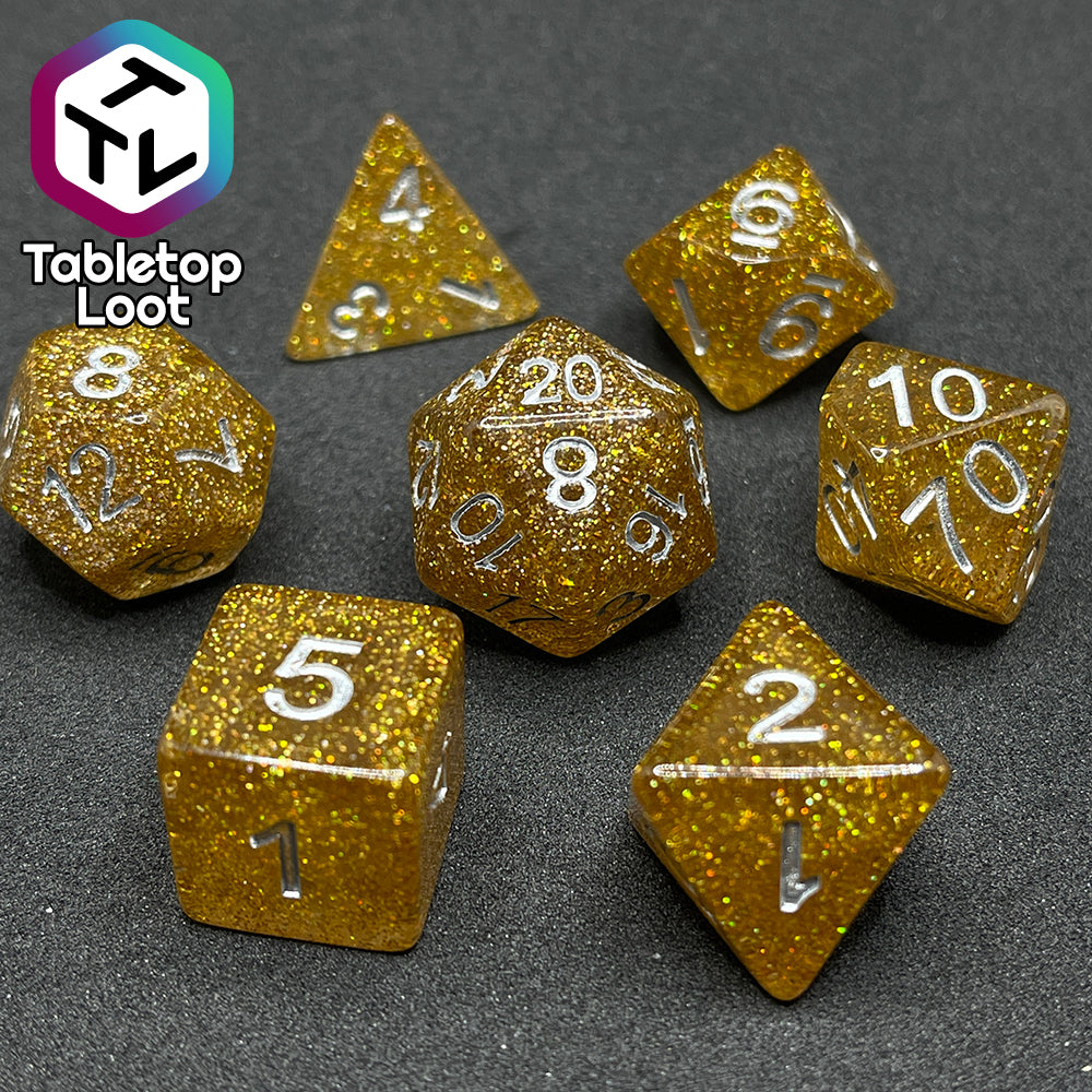 A close up of the Pixie Dust 7 piece dice set from Tabletop Loot; gold glittery dice with silver numbering.