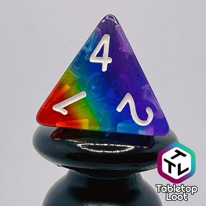 A close up of the D4 from the Pride 7 piece dice set from Tabletop Loot with stripes of translucent colors in rainbow order and white numbering.