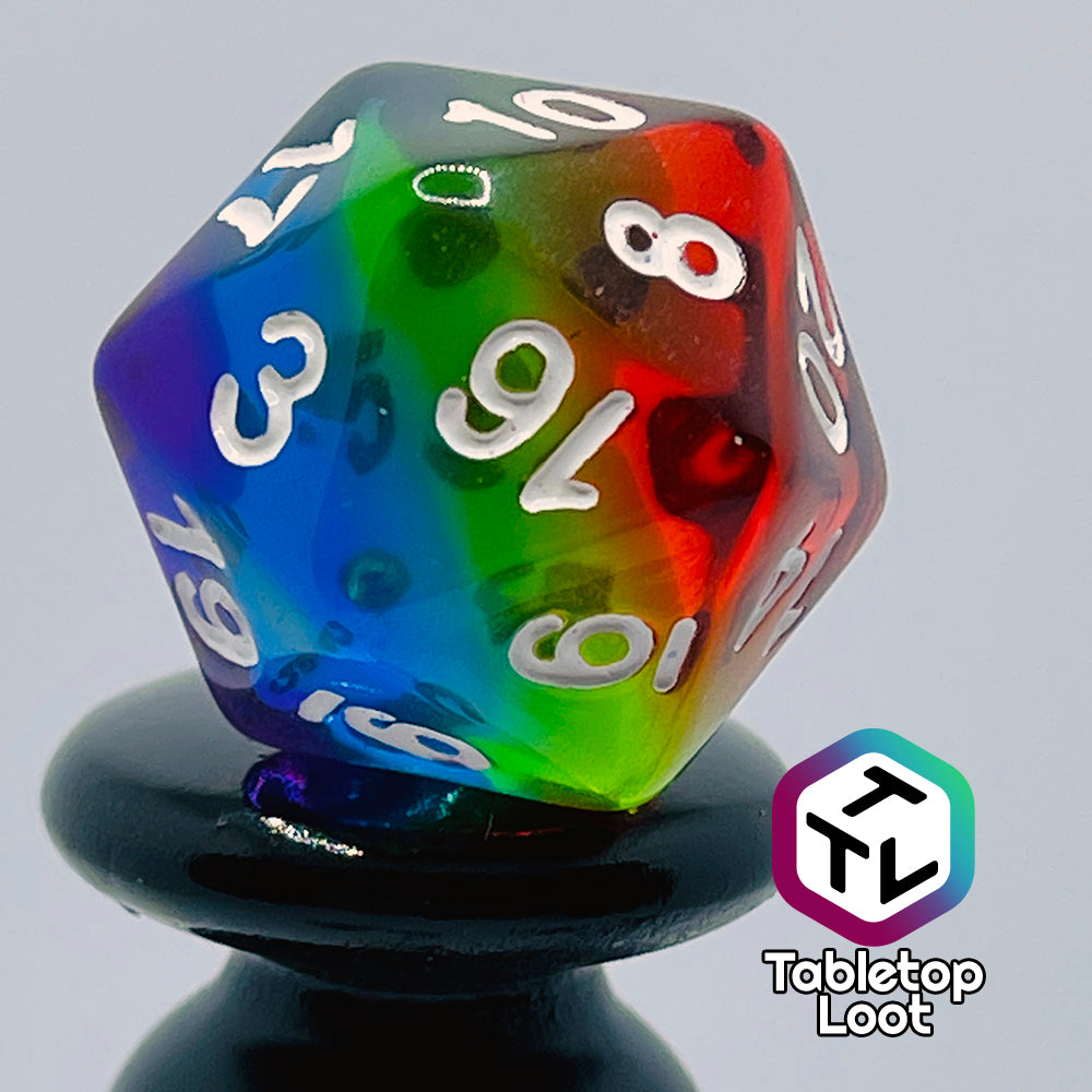 A close up of the D20 from the Pride 7 piece dice set from Tabletop Loot with stripes of translucent colors in rainbow order and white numbering.