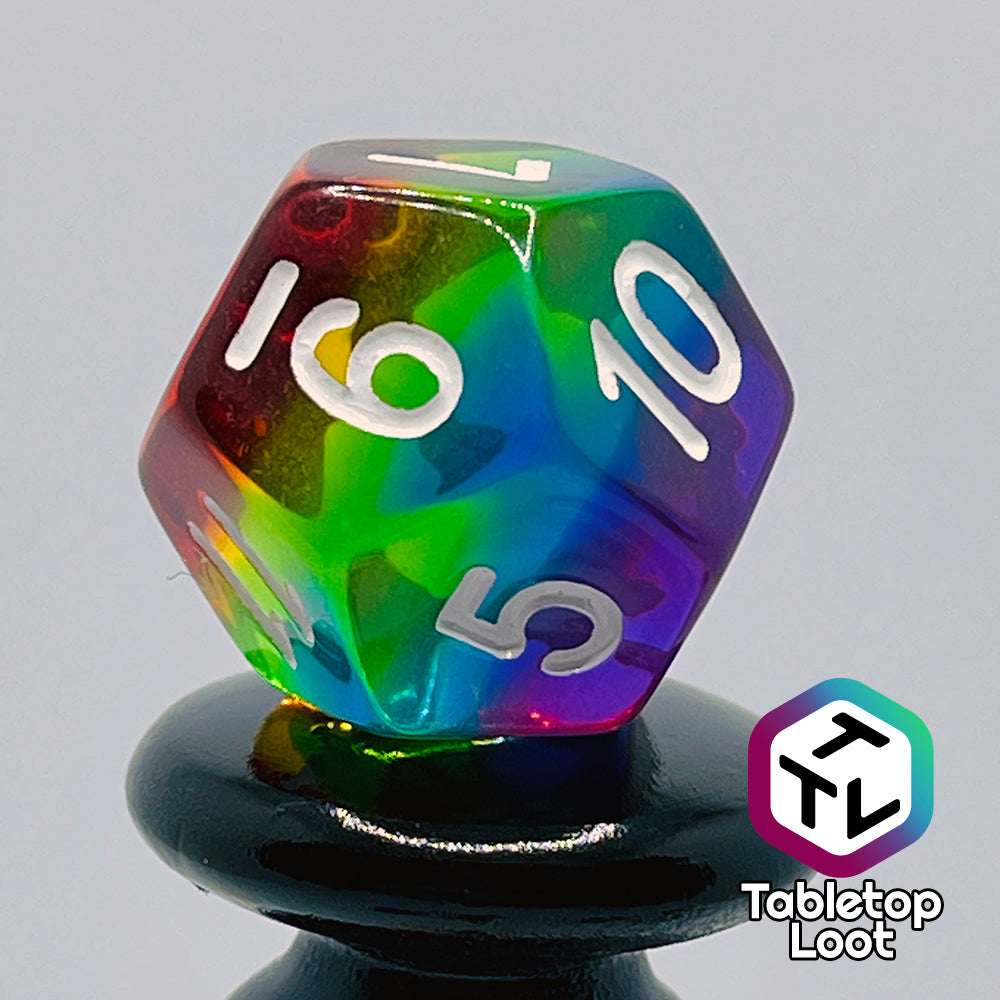 A close up of the D12 from the Pride 7 piece dice set from Tabletop Loot with stripes of translucent colors in rainbow order and white numbering.