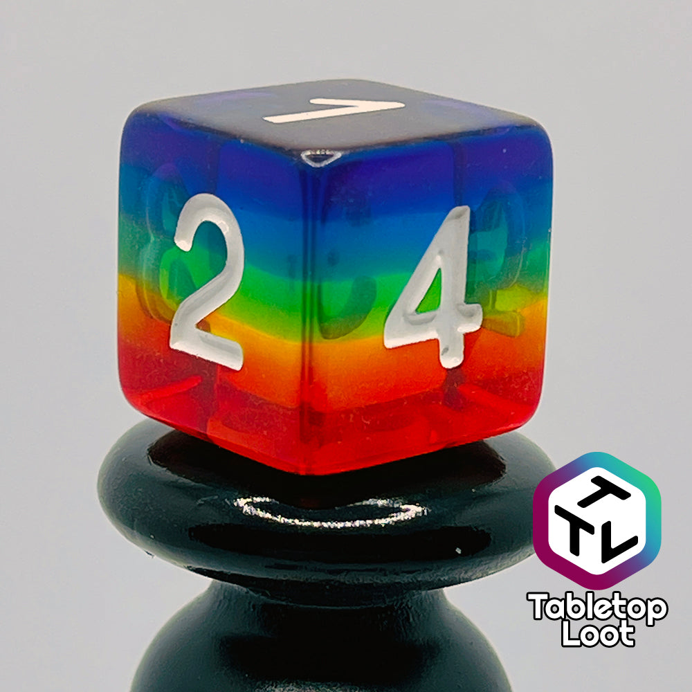 A close up of the D6 from the Pride 7 piece dice set from Tabletop Loot with stripes of translucent colors in rainbow order and white numbering.
