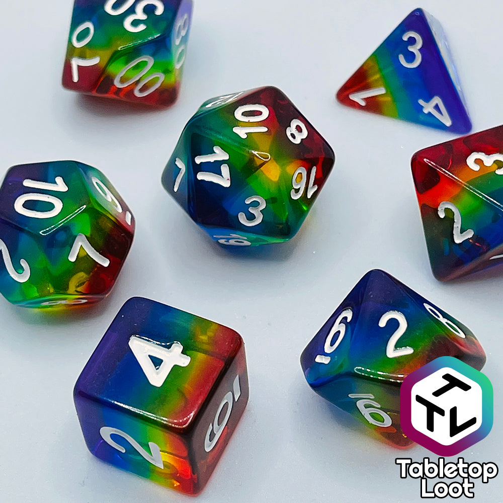 A close up of the Pride 7 piece dice set from Tabletop Loot with stripes of translucent colors in rainbow order and white numbering.