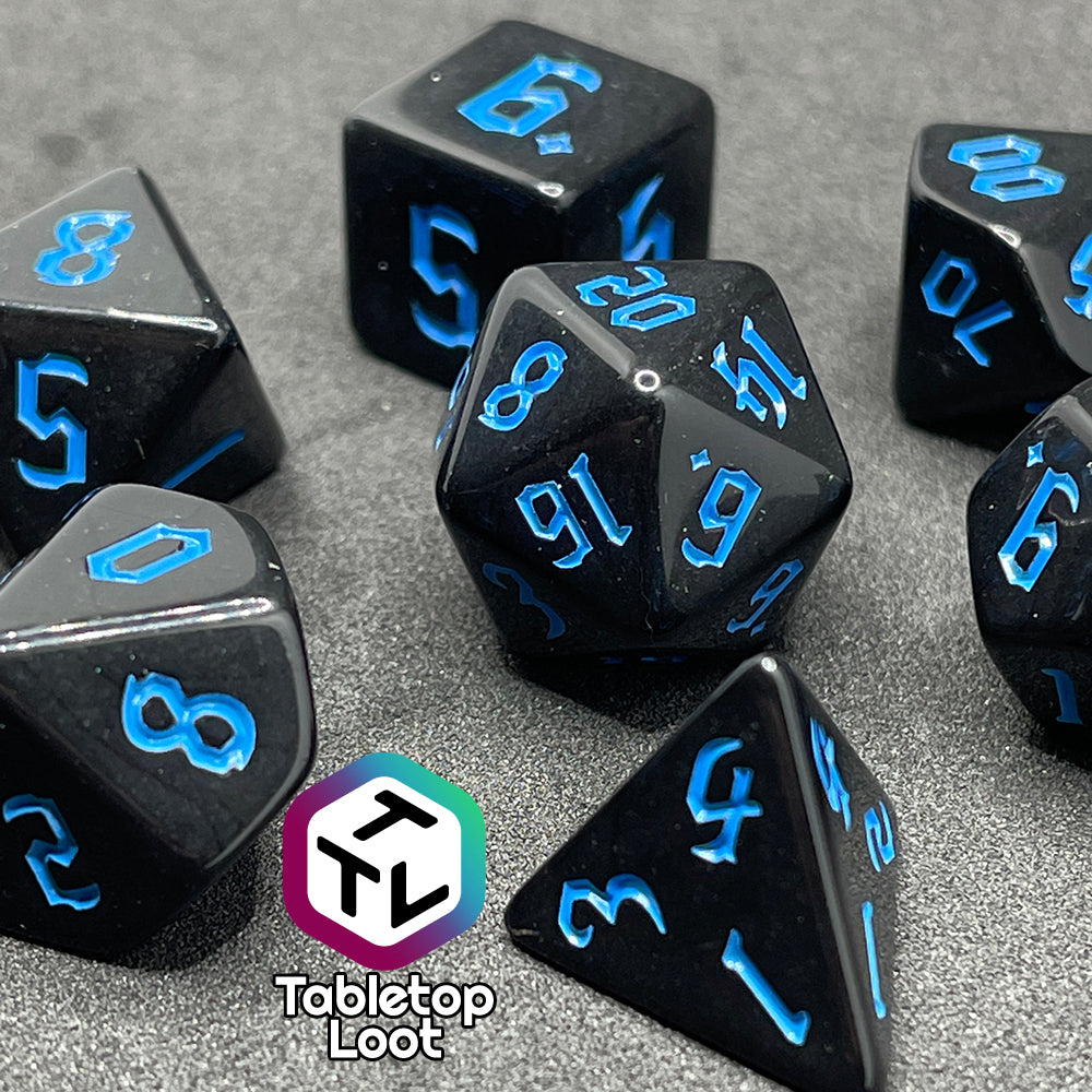 A close up of the Prime Directive 7 piece dice set from Tabletop Loot with bright blue bold gothic numbers on highly reflective black faces.