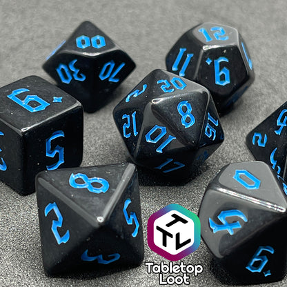 A close up of the Prime Directive 7 piece dice set from Tabletop Loot with bright blue bold gothic numbers on highly reflective black faces.