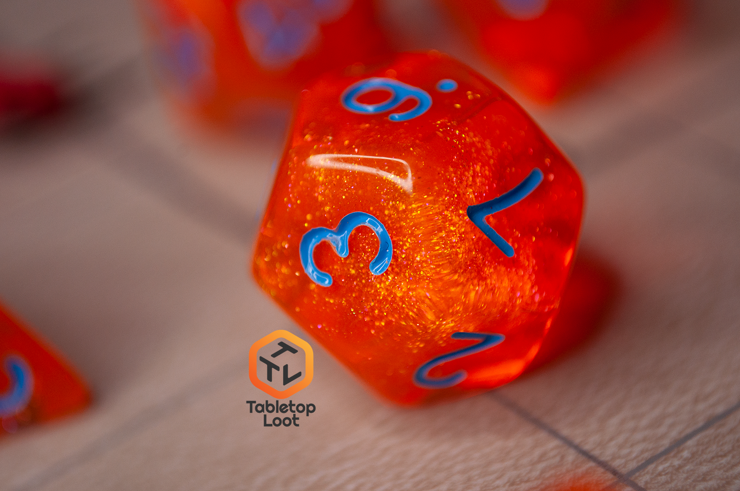 A close up of the D12 from the Radioactive Orange 7 piece dice set from Tabletop Loot with sparkly orange resin and bright blue numbering.