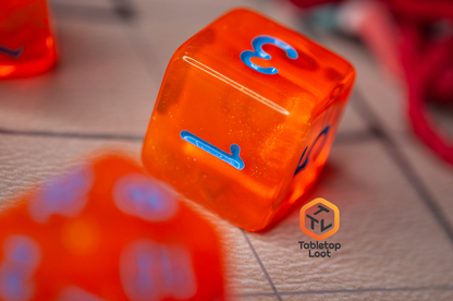 A close up of the D6 from the Radioactive Orange 7 piece dice set from Tabletop Loot with sparkly orange resin and bright blue numbering.